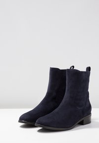 Bottines en daim bleu marine à talon bas carré, bout effilé, et languette à l'arrière ; texture lisse sans motifs visibles.