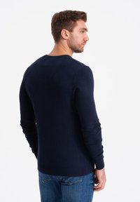 Marinblå långärmad tröja med rund halsringning samt ribbade ärmslut och nederkant, kombinerad med blå jeans. Slät textur och figursydd design.