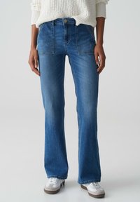 Blauwe denim flared jeans met een middelhoge taille, twee voorkruiden en een vervaagde afwerking. Gecombineerd met witte sneakers en een off-white gebreide trui.