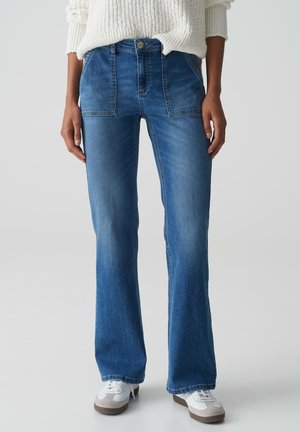 Blauwe denim flared jeans met een middelhoge taille, twee voorkruiden en een vervaagde afwerking. Gecombineerd met witte sneakers en een off-white gebreide trui.