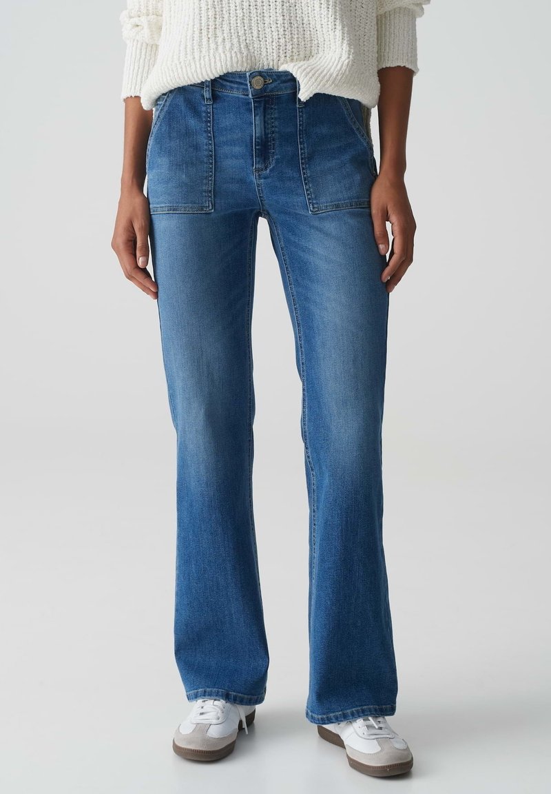 Blauwe denim flared jeans met een middelhoge taille, twee voorkruiden en een vervaagde afwerking. Gecombineerd met witte sneakers en een off-white gebreide trui.