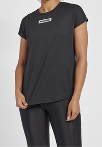 Black short-sleeve sports shirt in a smooth fabric with a rounded hem and a small white "HUMMEL" logo on the chest.