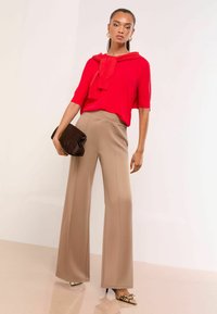 Red short-sleeve top with a draped neckline, paired with beige wide-leg trousers. Model holds a dark brown clutch. Snake-print heels.