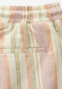 Primer plano de una tela a rayas en tonos beige, naranja, rosa y verde, con una cinturilla elástica y un bolsillo trasero horizontal.