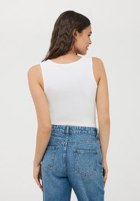 Top bianco senza maniche con scollatura rotonda, abbinato a jeans a vita alta blu chiaro con tasche e una texture in denim scolorito.