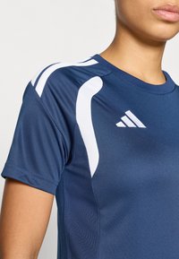 Μπλούζα απόδοσης του ναυτικού με κοντά μανίκια, που διαθέτει λευκές λεπτομέρειες και διχτυωτά πάνελ για αερισμό. Το λογότυπο Adidas εμφανίζεται στο στήθος.