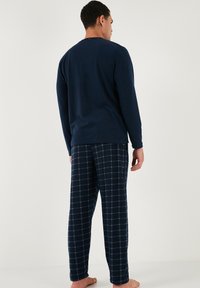 Mornarice dugih rukava u kombinaciji s mornarsko plavim i kariranim pidžama hlačama. Pamuk s mekim materijalom i opuštenim krojem.