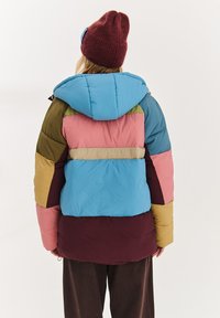 Vícebarevná péřová bunda s velkými záplatami v modré, růžové, zelené, hořčicové a vínové barvě, s kapucí a prošívanou texturou.