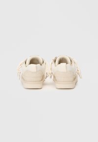 Sneaker beige con tessuto testurizzato e dettagli in suede, caratterizzati da un design low-top e linguette posteriori per una facile calzata.