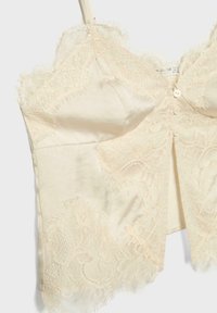 Caraco en satin crème orné de dentelle avec des boutons sur le devant et des bords délicatement festonnés sur les bretelles et l'ourlet.