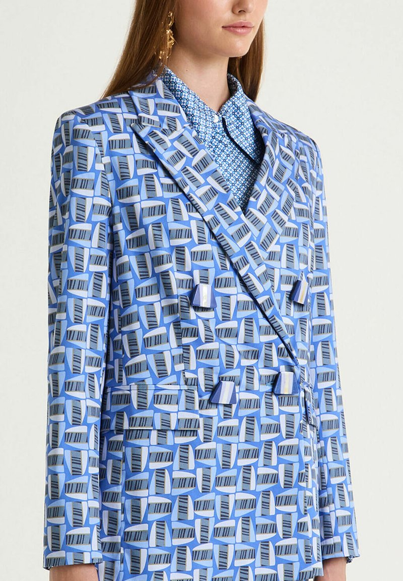 Blazer croisé bleu avec motif géométrique dans des nuances de bleu et de gris. Doté d'un col à revers et de rabats de poche.