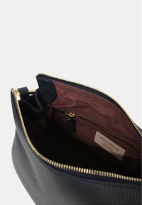 Borsa a tracolla nera in pelle con un'esterno testurizzato, zip dorata e una foderatura in tessuto marrone che presenta una tasca con zip e l'etichetta del marchio all'interno.