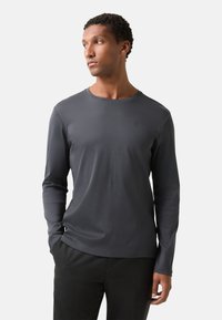 Tričko s dlouhým rukávem a kulatým výstřihem v tmavě šedé barvě, vyrobené z hladké látky. Obsahuje malé logo na hrudi a má přiléhavý střih.