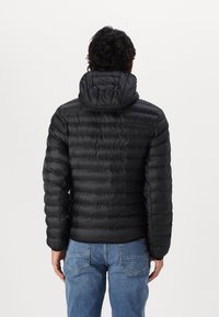 Černá péřová bunda s kapucí, s prošitým vzorem a hladkou texturou. Nositelná přes modré džíny, zobrazena zezadu.