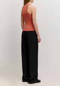Rote-orange körpernahe Tanktop mit Racerback-Design, kombiniert mit schwarzen weiten Hosen. Glatte Stofftextur und kontrastierende Farben.