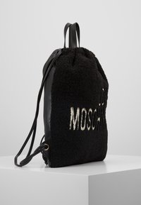 Svart ryggsäck med en plyschliknande, texturerad yta och läderbotten. Har en dragsko-stängning och broderad logotyp i vitt.