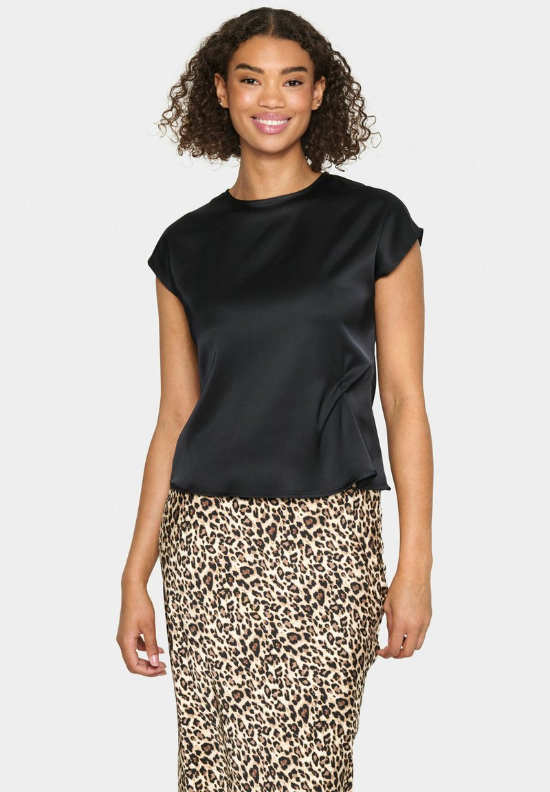 Top corto a maniche corte in satin nero con una texture liscia, abbinato a una gonna beige con stampa leopardata caratterizzata da macchie marroni scure e una silhouette aderente.