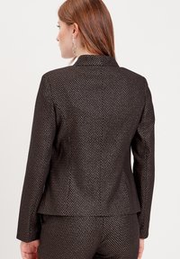 Black blazer with a textured pattern, featuring a single-button design, and a tailored fit. It has a smooth fabric and subtle sheen.