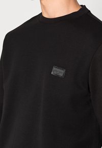 Felpa nera in cotone, con colletto rotondo e un'etichetta testurizzata sul petto. Tessuto liscio e vestibilità regolare.