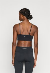 Μαύρο ενεργό αθλητικό σουτιέν με ρυθμιζόμενους ιμάντες, αδιάκοπη σχεδίαση και μικρό λογότυπο στην πλάτη. Συνδυάζεται με μαύρο κολάν ψηλόμεσο.