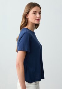 Marineblauwe T-shirt met korte mouwen, gemaakt van gladde stof, met een ronde hals en een relaxte pasvorm. Licht gebogen zoom, minimaal stiksel.