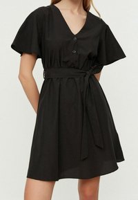 Robe noire à manches courtes, avec un décolleté en V, des détails de boutons et une ceinture à nouer. Fabriquée dans un tissu lisse avec une silhouette fluide.