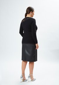 Schwarzer Pullover mit Spitzen-Details am Rücken, kombiniert mit einem schwarzen Leder-Bleistiftrock. Enthält silberne High Heels. Glatte Texturen.