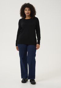 Zwarte lange mouw top met een ronde halslijn, gecombineerd met rechtvallende donkerblauwe spijkerbroek en zwarte plateau schoenen. Soepele stof textuur.