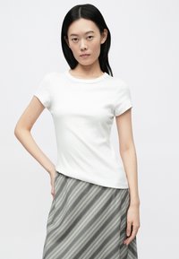 Hvid ribbet t-shirt med korte ærmer og rund halsudskæring, kombineret med en lang grå og hvidstribet nederdel. Glat tekstur og tætsiddende pasform.