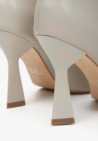 Szare skórzane buty na wysokim obcasie mają stożkowy obcas z jasnobrązowym akcentem. Gładka faktura z subtelnym detalem szwów.