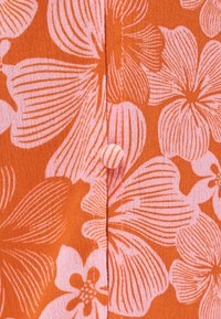 Tissu orange avec de grands motifs floraux roses et un bouton recouvert de tissu sur la couture centrale.