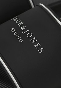Sandale flip-flop noire avec bordure blanche comportant un logo en relief blanc "JACK & JONES STUDIO" sur la bride.
