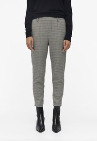 Pantalons à carreaux en beige et noir, coupe ajustée, avec une texture lisse, présentant des plis à l'avant et des poches latérales, associés à des bottines noires.