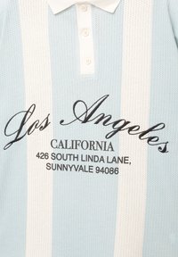 Svetle modré polo tričko s bílými pruhy, vyrobené z texturované látky. Má bílý límec a černý vyšívaný text s adresou.