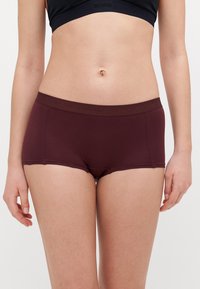 Shorts en coton stretch bordeaux avec un design sans coutures et une taille élastique. Présente un imprimé logo sur la ceinture.