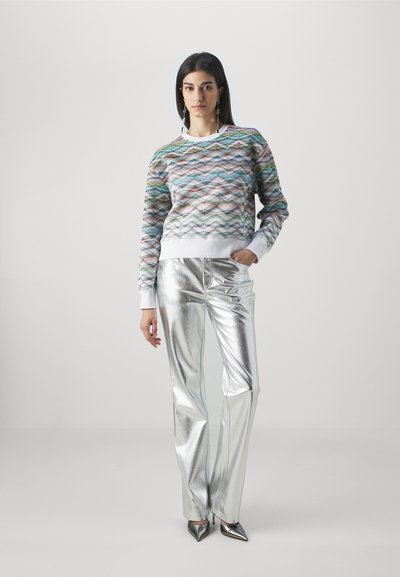 Πολύχρωμο πουλόβερ με σχέδιο κυμάτων και λευκό λαιμόκοψη, συνδυασμένο με γυαλιστερά ασημένια παντελόνια σε ευρεία γραμμή και μυτερά μεταλλικά τακούνια.