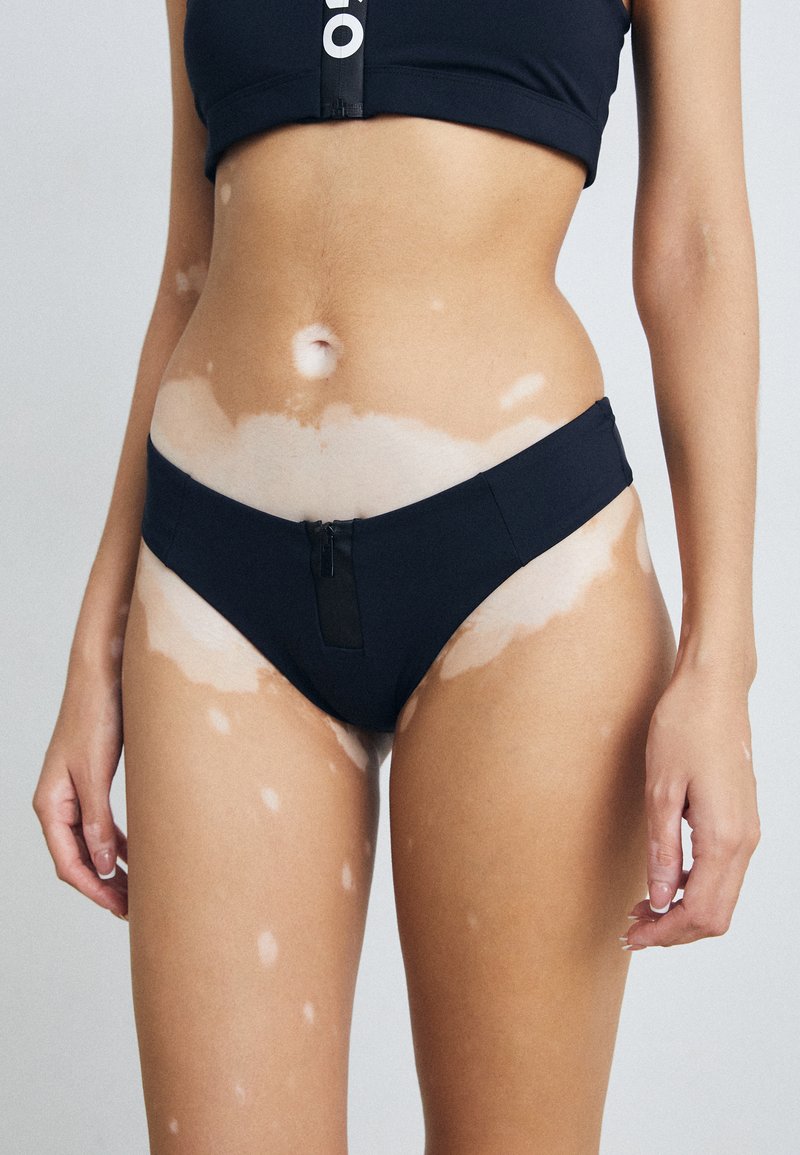 Juodas maudymosi bikini kostiumėlis su priekiniais užtrauktuko detalėmis. Pagamintas iš lygios, elastingos medžiagos. Minimalistinis dizainas su žemu juosmeniu.