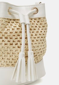 Bolso de bucket tejido en color beige con detalles en cuero blanco, que presenta un cierre de cordón y borlas decorativas en el extremo de las asas.