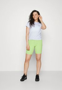 Lys grå T-skjorte med korte ermer, kombinert med tettsittende, knelengde, lysegrønne shorts og svarte trening-sko.