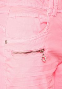 Primer plano de unos pantalones de tela rosa que muestran un bolsillo frontal con una cremallera plateada y un tirador de cremallera redondo.