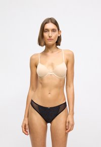 Beige gepadded bh met dunne bandjes, gecombineerd met zwarte low-rise bikini slips met een sprankelende textuur en netaccenten aan de zijkanten.