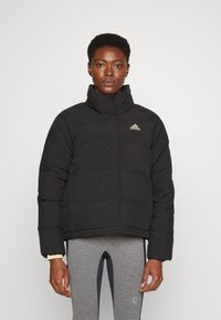 Czarna kurtka puchowa z wysokim kołnierzem, z pikowanym wzorem i haftowanym logo na lewym boku klatki piersiowej.