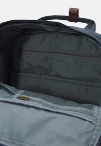 Blauw stoffen rugzakinterieur met een ritszak, zijvakken en een gladde textuur met subtiele merkpatronen.
