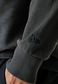 Felpa verde scuro con polsini a costine, caratterizzata da un tessuto testurizzato e un piccolo logo nero ricamato sulla manica.