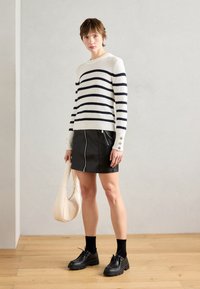 Hvit og marineblå stripete strikkegenser, svart skinn miniskjørt med frontglidelås, svarte snørebukser, og beige skulderveske.