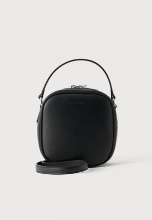 Petit sac à main ovale noir avec fermeture éclair argentée, poignée courte sur le dessus et longue bandoulière amovible, posé sur un fond uni clair.
