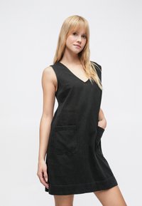 Čierne rifľové šaty bez rukávov s výstrihom do V, dvoma prednými vreckami a voľným strihom. Majú lem, ktorý siaha nad kolená.