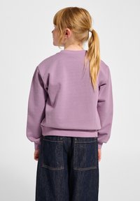 Lichtpaarse sweatshirt met geribbelde ronde hals en manchetten, gecombineerd met donkere denim broek met achterzakken en zichtbare stiksels.