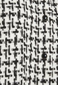 Svart och vit vävd textil med ett geometriskt mönster, som har en slät svart knappdetalj. Texturen verkar grov med synliga trådar.