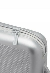 Funda dura plateada con un patrón texturizado de panal, cremallera blanca y una etiqueta con "Havaianas" grabada en ella. Diseño compacto.